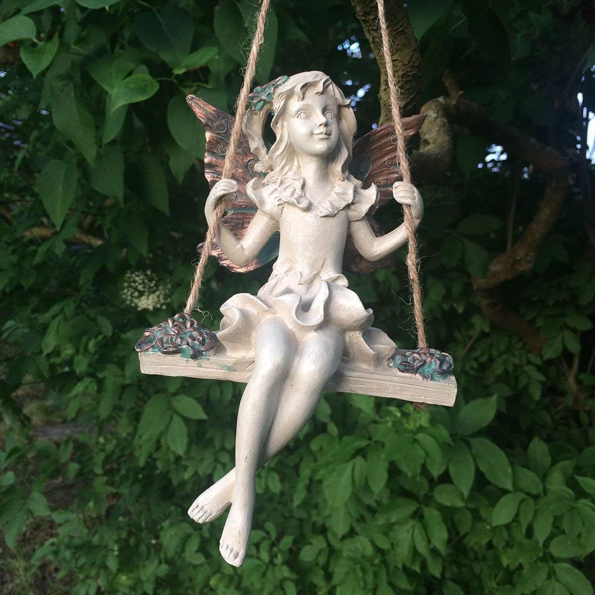 Statue of a fairy on a swing against a green leafy background
