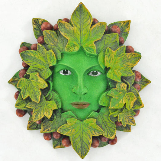 A decorative green tree of life wall plaque featuring a stylized human face surrounded by leaves and small berries, shown against a plain white background.