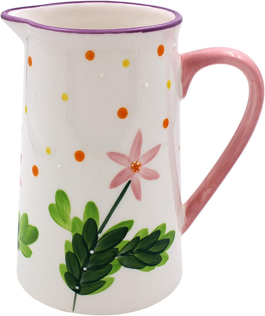 A white ceramic pitcher with a pink handle, decorated with a pink flower, green leaves, and orange and yellow polka dots, on a white background.