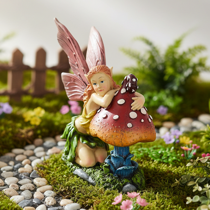 Fairy figurine sitting on a mushroom in a miniature garden setting with a wooden fence and flowers.