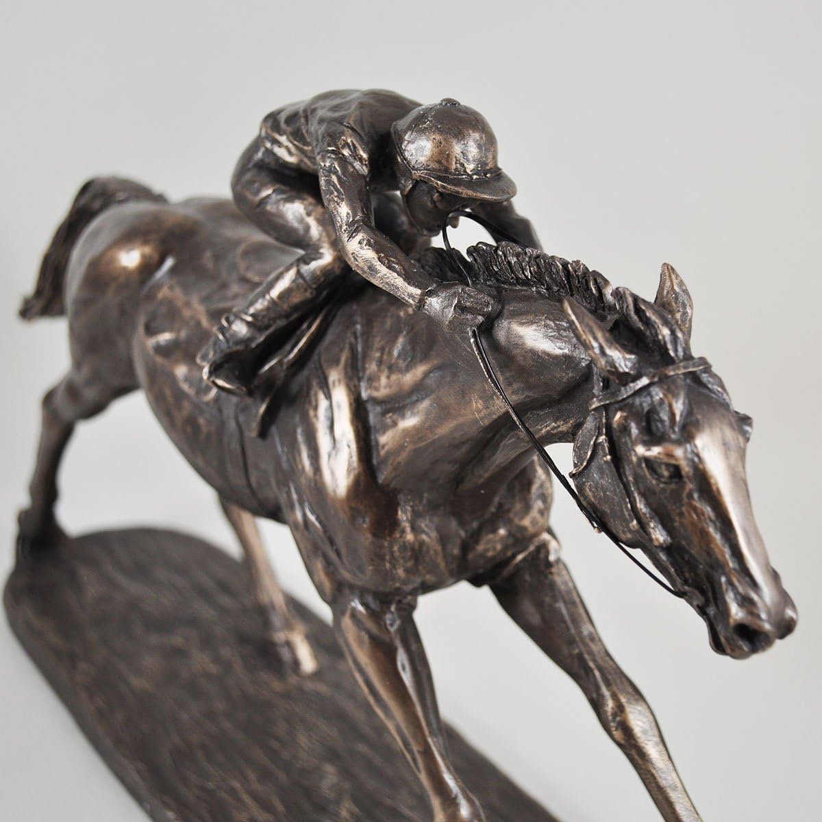 Bronze sculpture of a jockey on a horse against a gray background