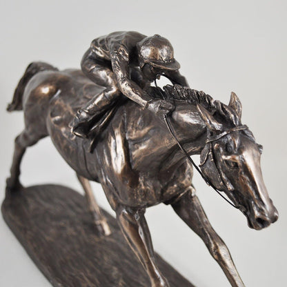 Bronze sculpture of a jockey on a horse against a gray background