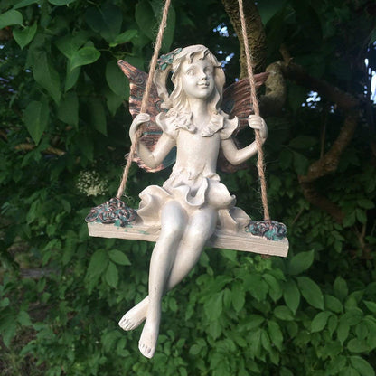 Statue of a fairy on a swing against a green leafy background