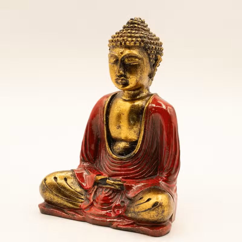 A seated Buddha statue with a gold-toned finish and red draped robes, photographed against a plain light background.
