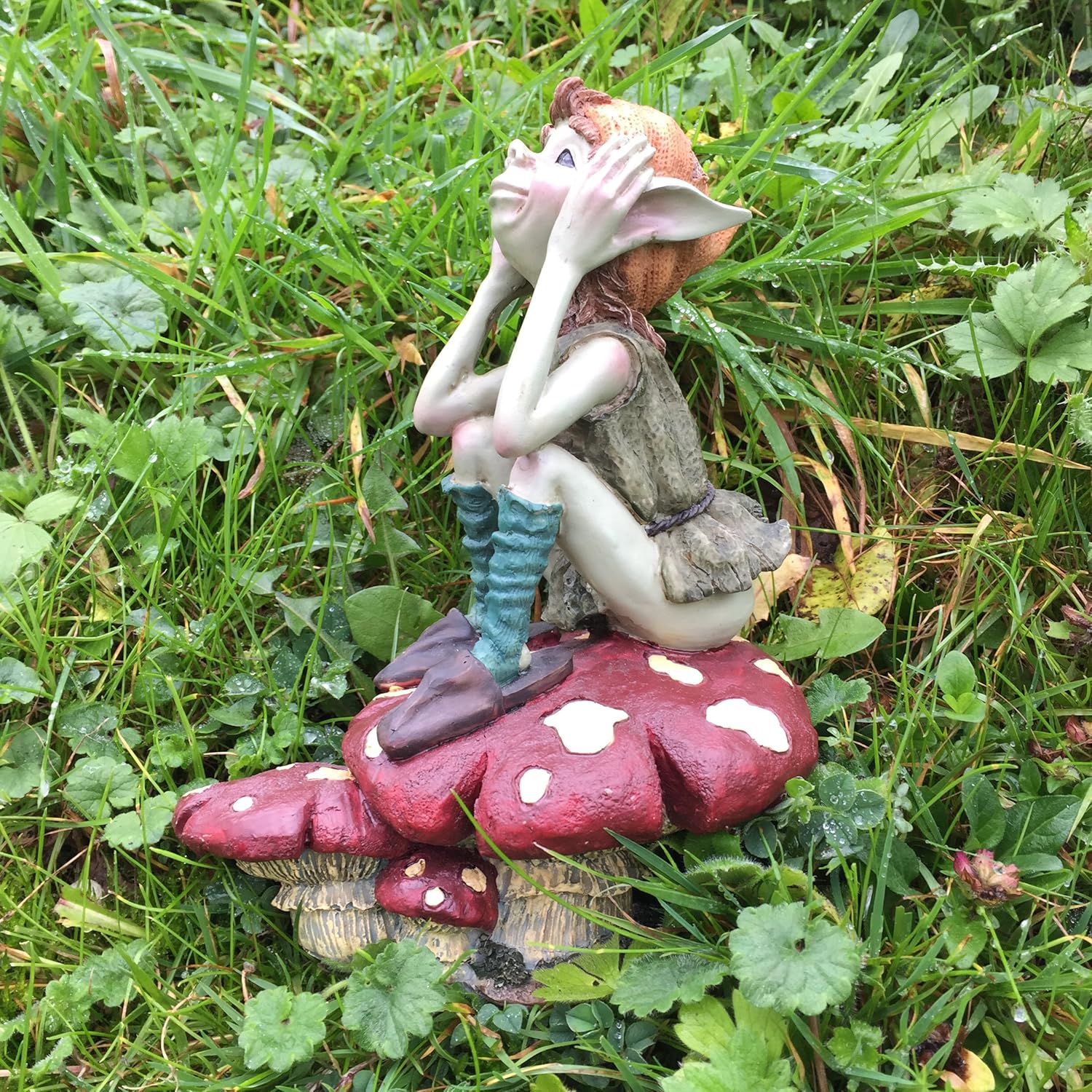 Gnome figurine sitting on a mushroom in a grassy area